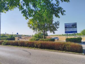 Eine Blick über die Straße auf die Baustelle mit der Bautafel.