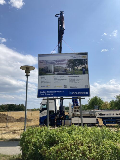 Die Bautafel wird mit einem Kran aufgestellt.