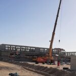 2023-10-11 Neubau 00002 Ein Autokran mit einem zweistöckigen Rohbau im Hintergrund.