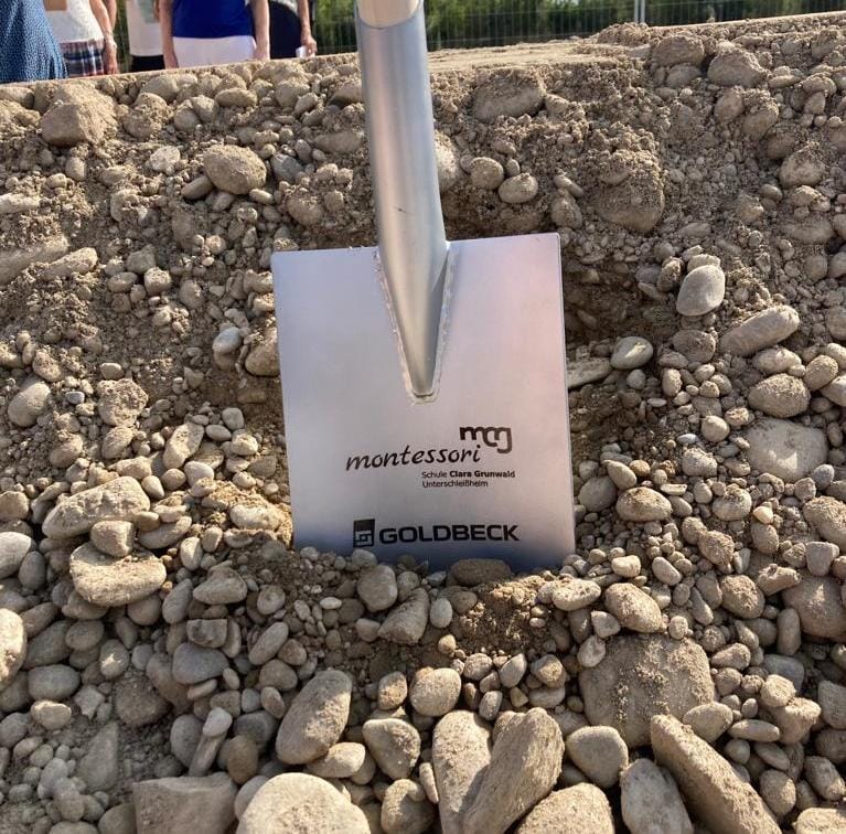 Spaten mit Aufschrift der Schule und der Baufirma steckt im Boden.