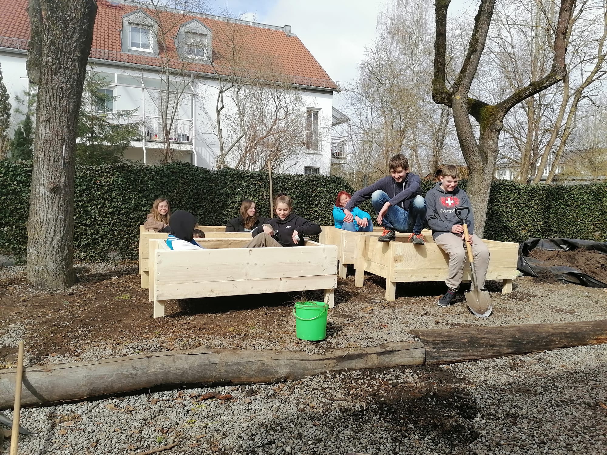 Jugendliche sitzen in neu gebauten Hochbeetkisten.