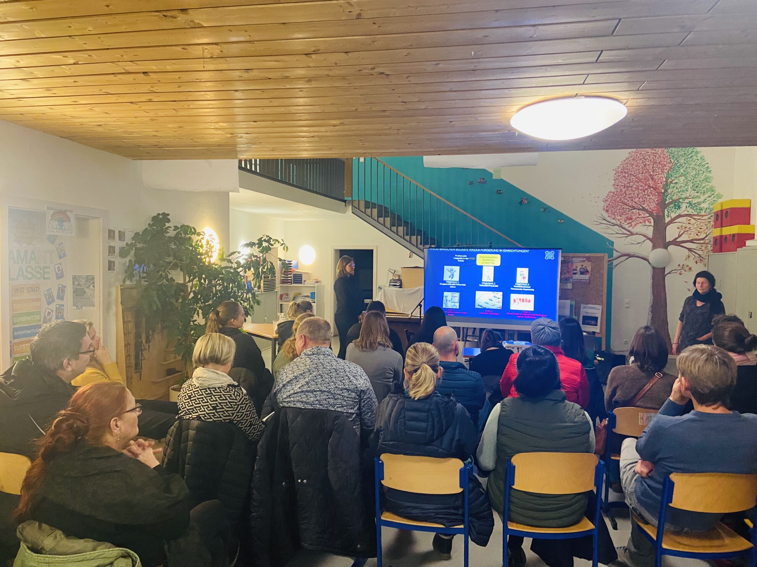 Eltern sitzen in der Aula bei einem Vortrag mit Präsentation.